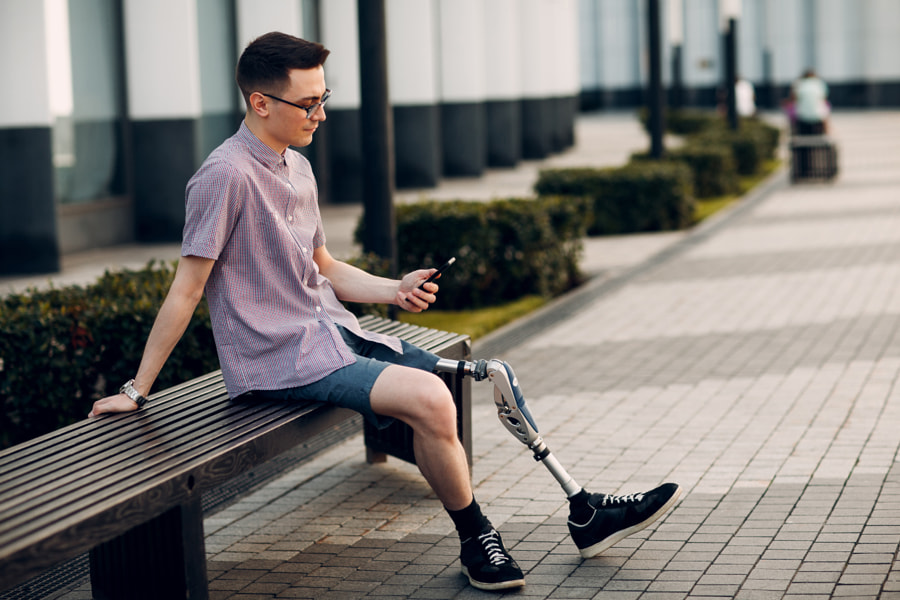 Jeune homme handicapé avec une prothèse de pied assis sur un banc en ville par Max Chernishev sur 500px.com
